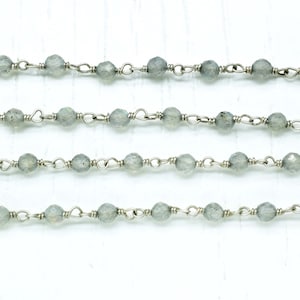 May include: A silver chain with grey gemstone beads. The chain is made of small, delicate links and the beads are round and smooth.