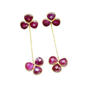 May include: A pair of gold earrings with three ruby-colored stones on each earring. The stones are connected by a gold chain.