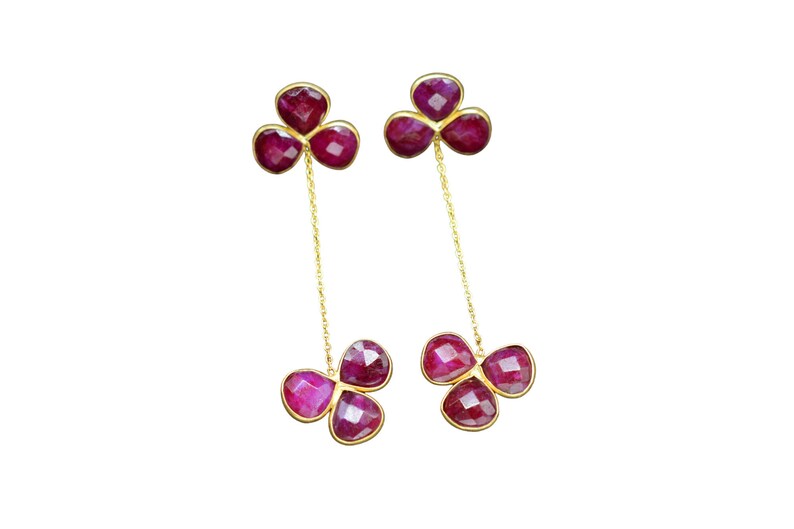 May include: A pair of gold earrings with three ruby-colored stones on each earring. The stones are connected by a gold chain.