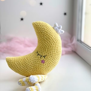 Cute handmade crochet moon plush made with soft velvet yarn, sleeping crescent moon amigurumi toy on a windowsill, cozy nursery decor, kawaii moon pillow for baby room.