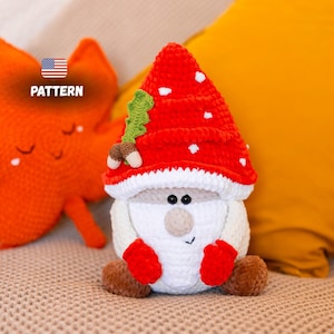 May include: A handmade crochet gnome doll with a red mushroom cap with white spots, a white beard, and red mittens. The doll has black eyes and a small nose. The word "PATTERN" is visible in the image.