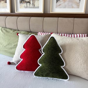 Può includere: Due cuscini decorativi a forma di albero di Natale, uno rosso tinta unita e uno verde scuro tinta unita, entrambi caratterizzati da un bordo spesso lavorato all'uncinetto bianco. I cuscini presentano una trama visibile e una forma triangolare.