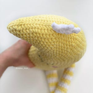 May include: A handmade yellow crochet moon plush toy with a white cloud accent. The moon has a smiling face and striped yellow and white legs. The toy is soft and cuddly, perfect for a child's room or nursery.