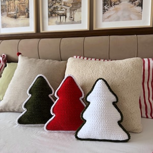 Könnte beinhalten: Drei dekorative Kissen in Form von Weihnachtsbäumen, jedes mit einer gehäkelten Textur. Ein Kissen ist dunkelgrün mit weißem Rand, eines ist hellrot mit weißem Rand und eines ist weiß mit einem dunkelgrünen Rand.