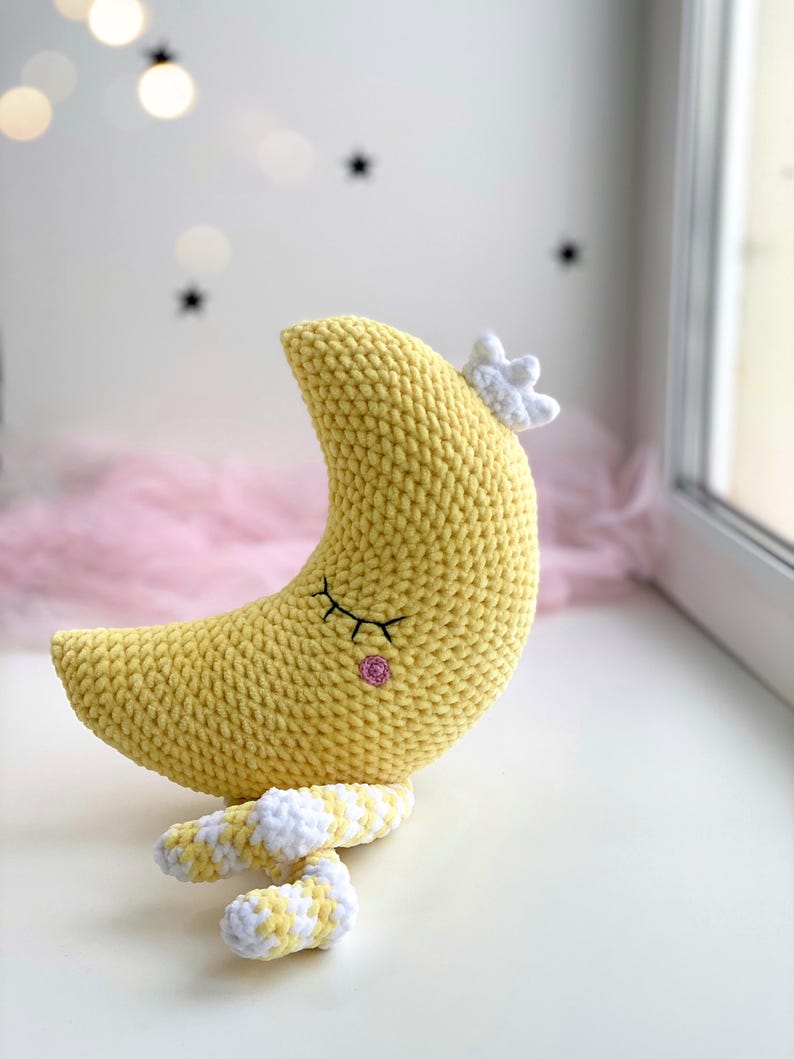 Cute handmade crochet moon plush made with soft velvet yarn, sleeping crescent moon amigurumi toy on a windowsill, cozy nursery decor, kawaii moon pillow for baby room.