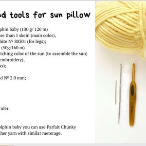 May include: Materials and tools for crocheting a sun pillow. The image shows a skein of yellow yarn, two crochet hooks, a tapestry needle, a stitch marker, a measuring tape, and small balls of yarn in black, pink, and yellow.