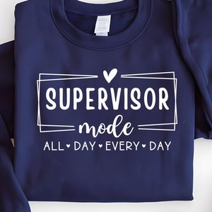 Puede incluir: Una sudadera azul marino con texto blanco que dice "SUPERVISOR mode ALL DAY EVERY DAY" con un pequeño corazón sobre la palabra "SUPERVISOR".