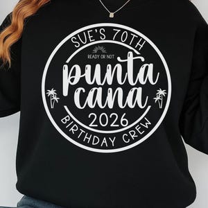 May include: Black sweatshirt with a white circular graphic. The graphic reads "Sue's 70th Punta Cana 2026 Birthday Crew" with palm tree and sun illustrations. The text "Ready or Not" is above "Punta Cana".