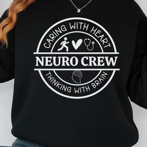 May include: Black sweatshirt with a white circular graphic that reads "Caring with Heart, Neuro Crew, Thinking with Brain." The graphic includes a running figure, a heart, a stethoscope, and a brain illustration. The sweatshirt has long sleeves.