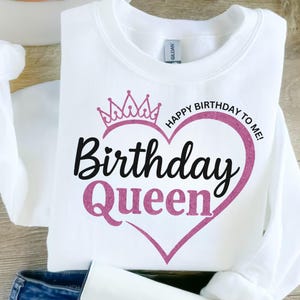 Może przedstawiać: Biała bluza z nadrukiem w kształcie różowego serca z brokatem, na którym widnieje napis "Happy Birthday to Me!" i "Birthday Queen" czarnym kolorem. Nad sercem znajduje się różowa korona z brokatem.