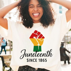 May include: White t-shirt with a raised fist graphic in red, yellow, and green colors. The text "Juneteenth Since 1865" is printed below the fist.
