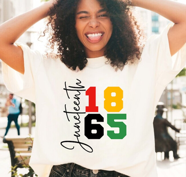 May include: A white t-shirt with the text "Juneteenth" and the numbers "1865" in red, yellow, black, and green.