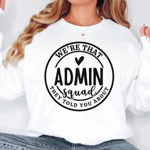 May include: White sweatshirt with the text "WE'RE THAT ADMIN squad THEY TOLD YOU ABOUT" in a black circular design. The sweatshirt has long sleeves and a crew neck. The text includes a heart symbol.