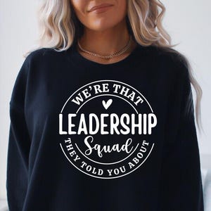 May include: Black sweatshirt with a white circle graphic that says "We're That Leadership Squad They Told You About" with a small heart in the center.
