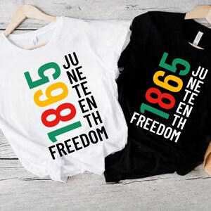 Peut inclure: Deux t-shirts, un blanc et un noir, chacun avec un graphisme coloré. Le graphisme comprend les chiffres "1865" en vert, jaune et rouge, et les mots "Juneteenth Freedom" en blanc.
