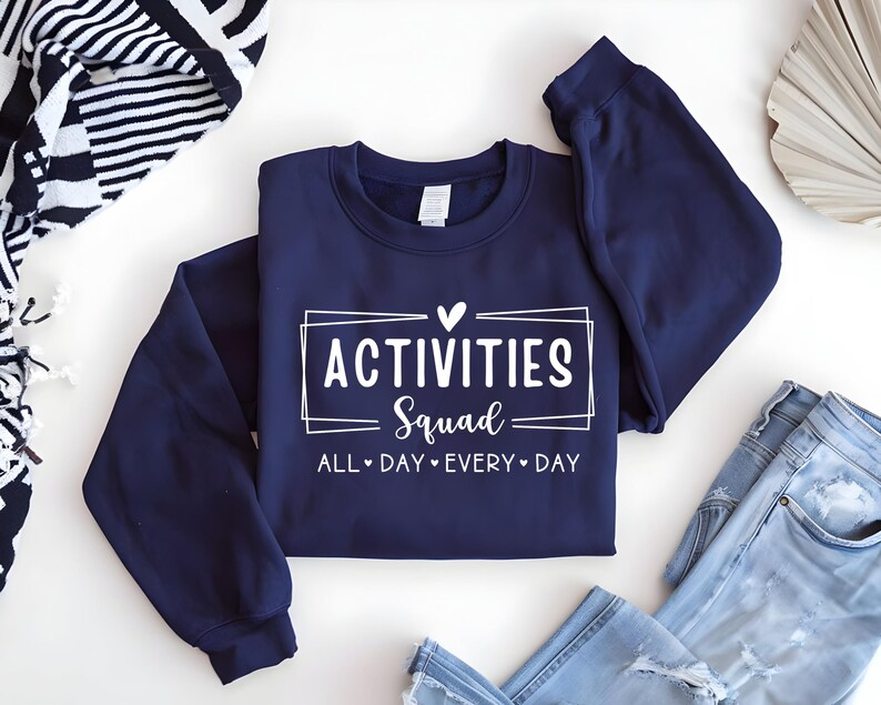 Op de afbeelding: Navyblauwe trui met witte tekst die "Activities Squad All Day Every Day" met een hartje zegt.