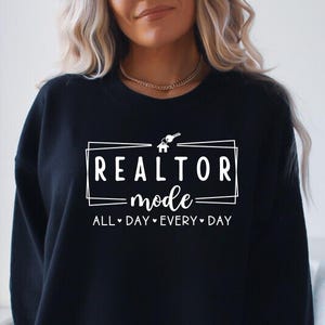 May include: Black sweatshirt with white text that reads "Realtor Mode All Day Every Day" with a house and key graphic.