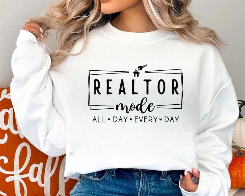 May include: White sweatshirt with black text that reads "Realtor Mode All Day Every Day" with a house and key graphic.