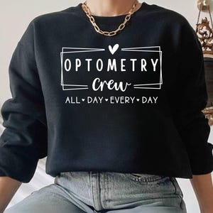 May include: Black sweatshirt with white text that reads "Optometry Crew" in a box with a heart above it. The text "All Day Every Day" is below the box.