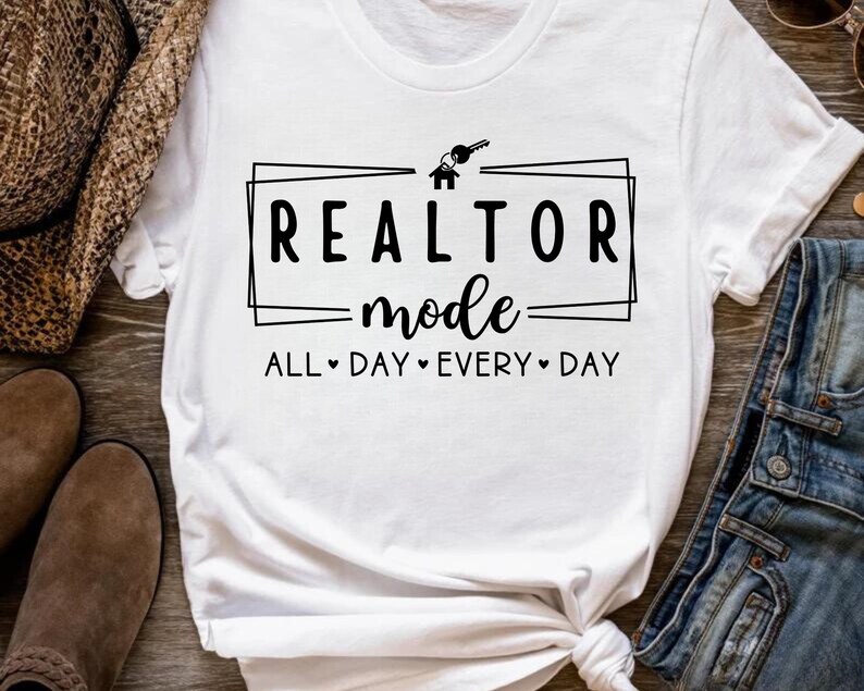 May include: White t-shirt with black text that reads "Realtor mode all day every day" with a house and key graphic above the text.