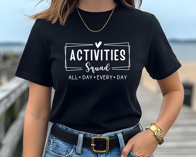 Op de afbeelding: Zwart T-shirt met witte tekst die "Activities Squad" zegt met een hartje en "All Day Every Day" eronder.