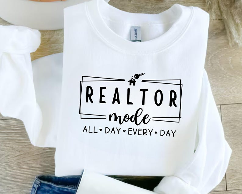 May include: White sweatshirt with black text that reads "Realtor Mode All Day Every Day" with a house and key graphic.