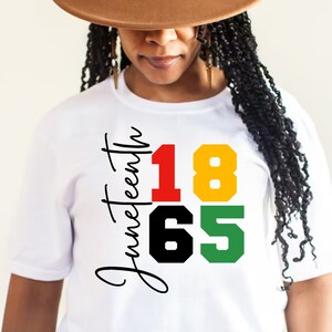 May include: White t-shirt with the text "Juneteenth 1865" in black, red, yellow, and green lettering.