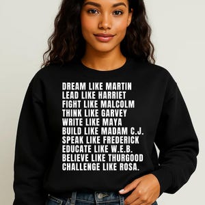 Peut inclure: Sweat-shirt noir avec texte blanc : "DREAM LIKE MARTIN, LEAD LIKE HARRIET, FIGHT LIKE MALCOLM, THINK LIKE GARVEY, WRITE LIKE MAYA, BUILD LIKE MADAM C.J., SPEAK LIKE FREDERICK, EDUCATE LIKE W.E.B., BELIEVE LIKE THURGOOD, CHALLENGE LIKE ROSA."