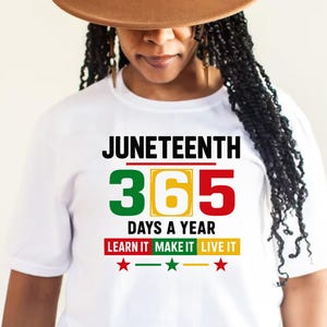 May include: White t-shirt with the text "Juneteenth 365 Days a Year Learn It Make It Live It" in black and red, yellow, and green lettering. There are three red stars below the text.