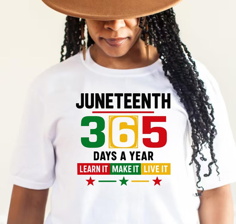 May include: White t-shirt with the text "Juneteenth 365 Days a Year Learn It Make It Live It" in black and red, yellow, and green lettering. There are three red stars below the text.