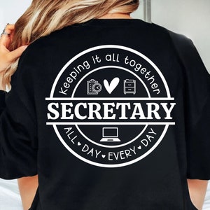 Può includere: Felpa nera con una grafica circolare bianca che dice "Keeping it all together SECRETARY all day every day" con icone di una clipboard, un cuore e un archivio.