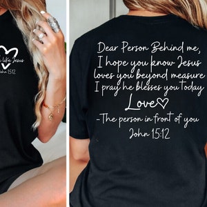 May include: Black t-shirt with white text that reads "Love like Jesus John 15:12" on the front and "Dear Person Behind me, I hope you know Jesus loves you beyond measure I pray he blesses you today Love♡ -The person in front of you John 15:12" on the back.