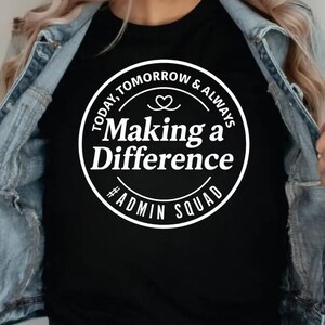 May include: Black t-shirt with a white circular graphic that reads "Today, Tomorrow & Always Making a Difference #Admin Squad". The shirt is worn with a light blue denim jacket.