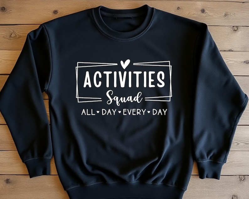 Op de afbeelding: Zwart sweatshirt met witte tekst die "Activities Squad" luidt met een hartje boven de tekst en "All Day Every Day" onder de tekst.
