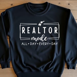 May include: Black sweatshirt with white text that reads "Realtor mode - All Day Every Day" with a house and key graphic.