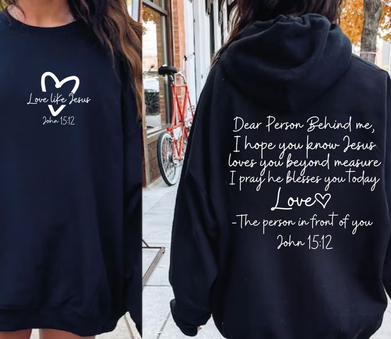 May include: Two black sweatshirts with white text. The front sweatshirt has a heart and the text "Love like Jesus John 15:12". The back sweatshirt has the text "Dear Person Behind me, I hope you know Jesus loves you beyond measure I pray he blesses you today Love♡ -The person in front of you John 15:12".