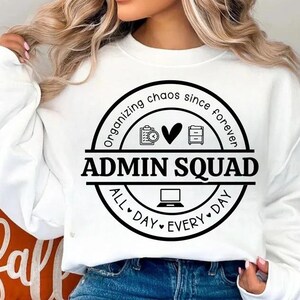 May include: White sweatshirt with a black circular graphic that reads "Organizing chaos since forever" and "Admin Squad All Day Every Day." The graphic includes icons of a clipboard, heart, file cabinet, and laptop.