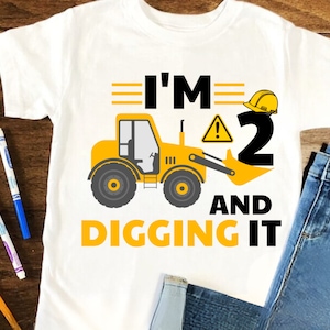 May include: A white t-shirt with a yellow construction vehicle and the text "I'm 2 and digging it".