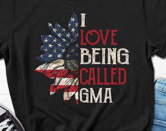 Op de afbeelding: Zwart T-shirt met een rood, wit en blauw zonnebloemontwerp. De tekst "Ik hou ervan om GMA genoemd te worden" staat op het shirt gedrukt.