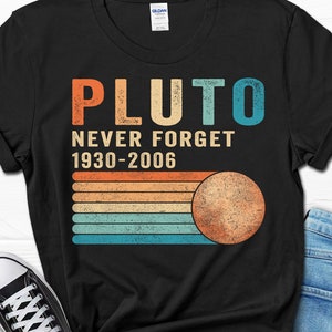 May include: Black t-shirt with a vintage-style graphic that says "Pluto Never Forget 1930-2006". The graphic features a stylized image of Pluto with a rainbow-colored background.