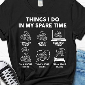 May include: A black t-shirt with white text that reads "Things I do in my spare time". The text is surrounded by six illustrations of trains, each with a caption describing a train-related activity. The captions are "Travel by trains", "Look at trains", "Research trains", "Talk about trains", "Think about trains", and "Dream about trains".