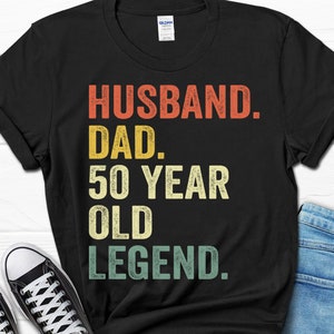 May include: Black t-shirt with a vintage-style graphic that reads "Husband. Dad. 50 Year Old Legend."