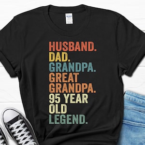 May include: Black t-shirt with a vintage-style graphic that reads "Husband. Dad. Grandpa. Great Grandpa. 95 Year Old Legend."
