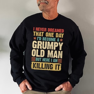 May include: Black sweatshirt with a vintage-style graphic that reads "I never dreamed that one day I'd become a grumpy old man but here I am killing it".