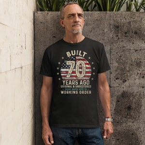 May include: Black t-shirt with a vintage American flag design and the text "BUILT 70 YEARS AGO ORIGINAL & UNRESTORED - most parts still in - WORKING ORDER".