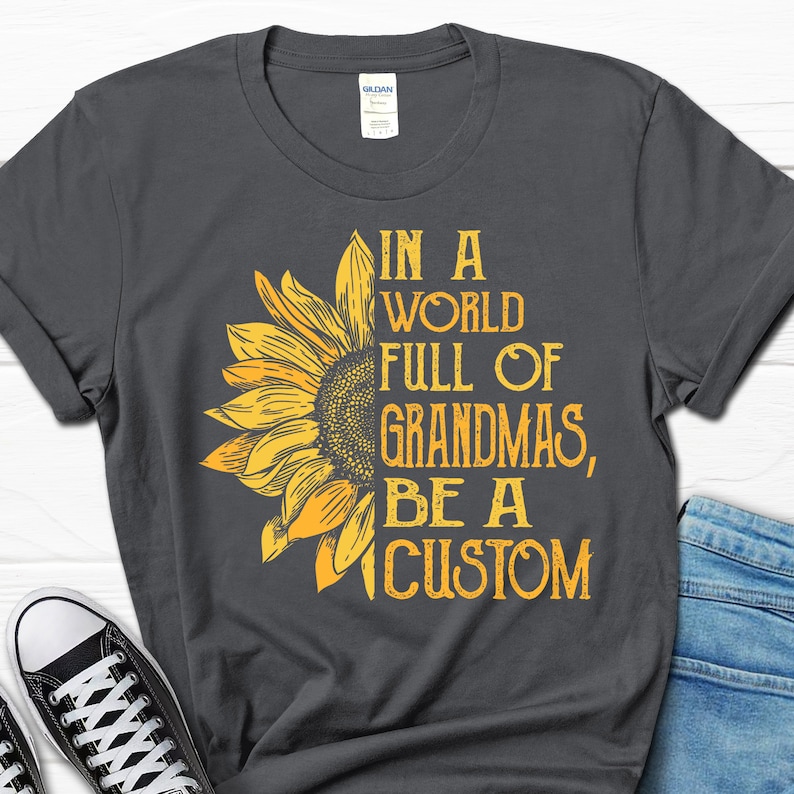May include: A dark grey t-shirt with a sunflower graphic and the text "In a world full of grandmas, be a custom".
