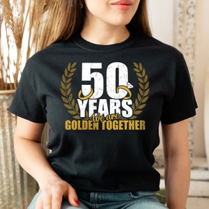 May include: Black t-shirt with a white graphic that says "50 Years We are Golden Together" with two gold rings and a laurel wreath.