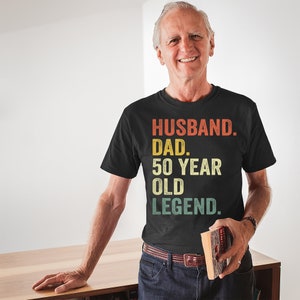May include: A black t-shirt with a vintage-style graphic that reads "Husband. Dad. 50 Year Old Legend."