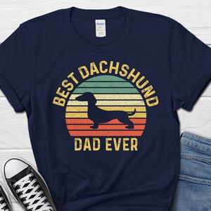 May include: Navy blue t-shirt with a vintage-style graphic of a dachshund and the text "Best Dachshund Dad Ever".