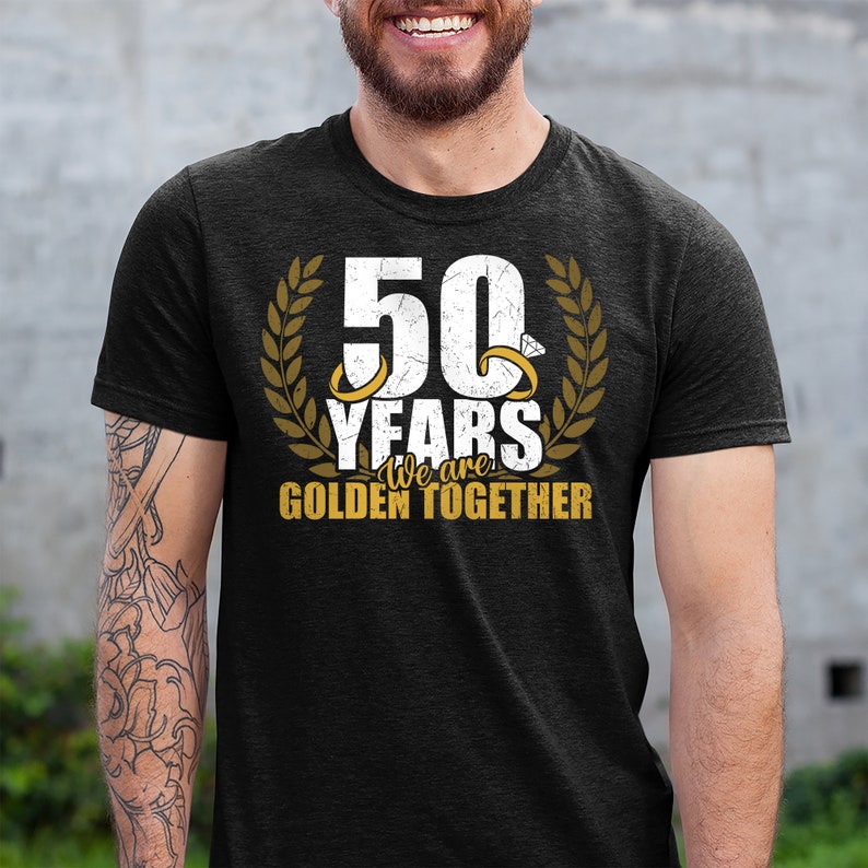 May include: A black t-shirt with a gold graphic that says "50 Years We are Golden Together" with two gold rings and a laurel wreath.